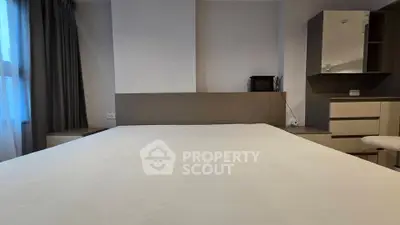 Spacious bedroom with modern furnishings and natural light from large window.
