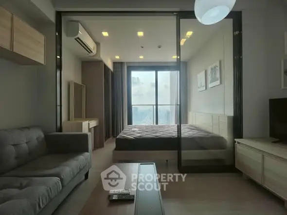 Modern apartment with glass partition, cozy living area, and city view from bedroom.
