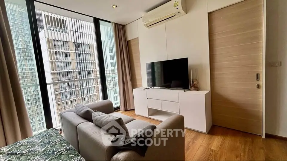 Modern living room with large windows and city view, featuring sleek furniture and wooden flooring.