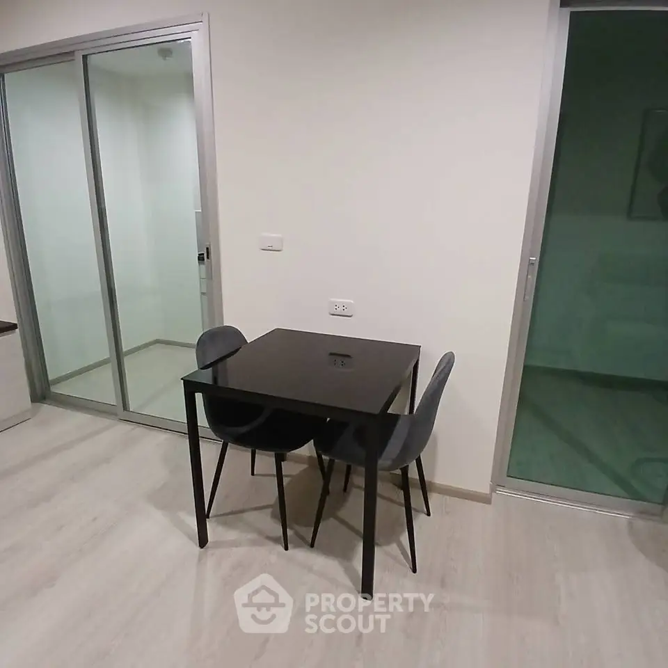 Modern minimalist dining area with sleek black table and chairs, adjacent to sliding glass doors.