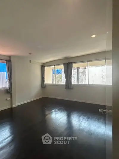 Spacious empty room with large windows and dark wooden flooring, ideal for customization.