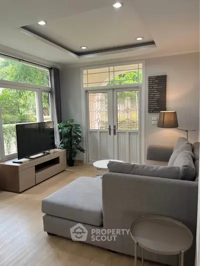 Charming living room with modern decor and large windows offering lush garden views.