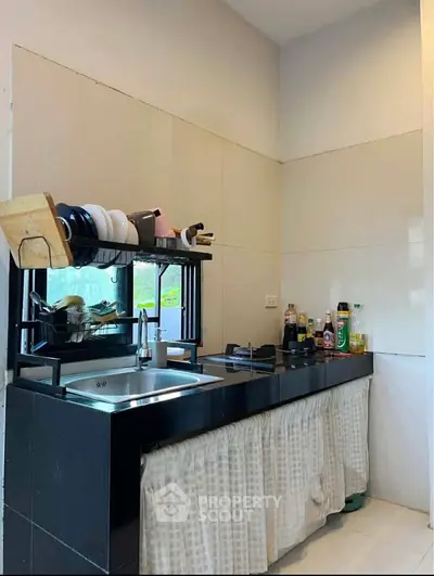 Modern kitchen with sleek black countertops and open shelving, featuring a gas stove and ample natural light.