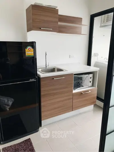 Modern compact kitchen with sleek wooden cabinets and black fridge