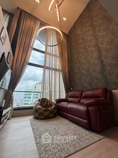 Modern living room with high ceilings and large windows, featuring a red leather sofa and stylish lighting.