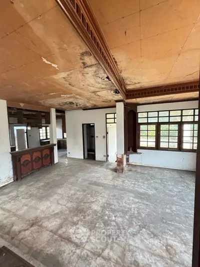 Spacious living room with vintage wooden accents and large windows, ideal for renovation.