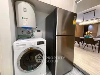 Modern kitchen with washing machine, fridge, and dining area in sleek apartment.