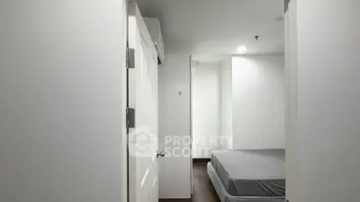 Minimalist bedroom with white walls and simple decor, featuring a bed and door.