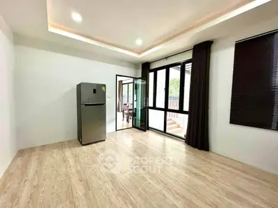 Spacious living room with modern fridge and large windows opening to a patio, perfect for entertaining.
