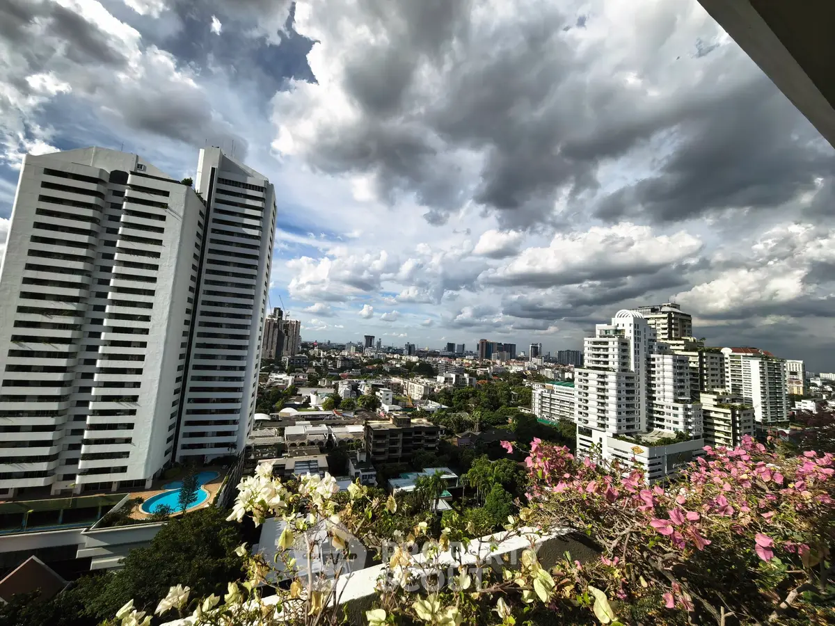 Stunning cityscape view from a high-rise balcony with lush greenery and dramatic clouds.