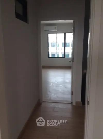 Spacious apartment hallway leading to a bright room with large windows.