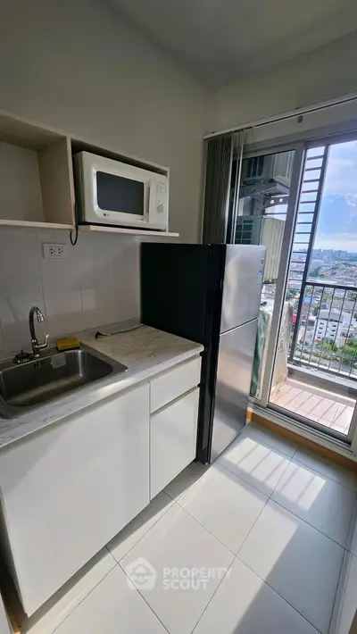 Compact kitchen with microwave, fridge, and balcony view in modern apartment