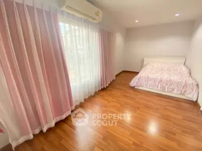 Spacious bedroom with wooden flooring and pink curtains, featuring a cozy bed and ample natural light.