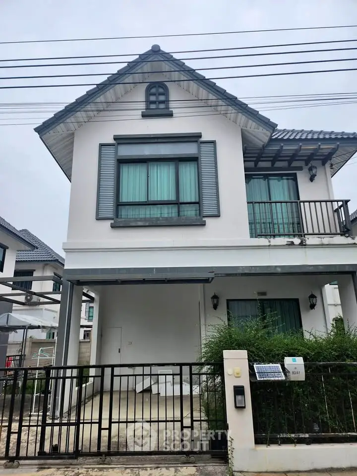 Charming two-story house with balcony and gated entrance in a serene neighborhood.