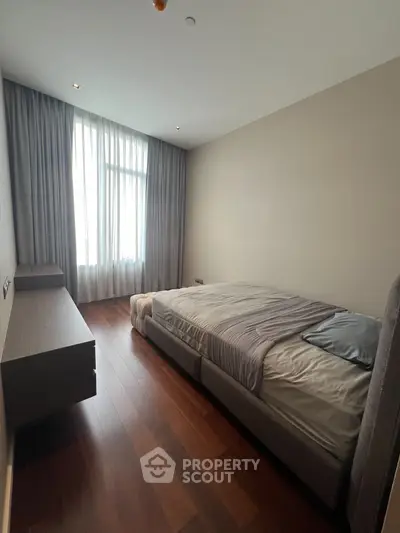 Spacious modern bedroom with wooden flooring and large window for natural light.