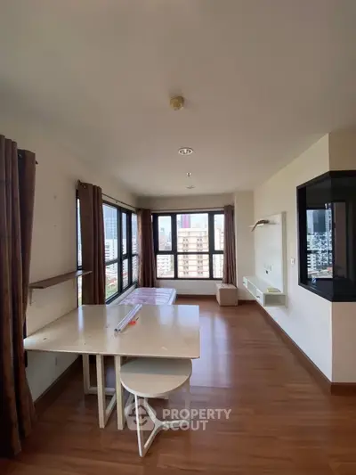 Spacious living room with large windows offering city views, featuring modern furniture and wooden flooring.