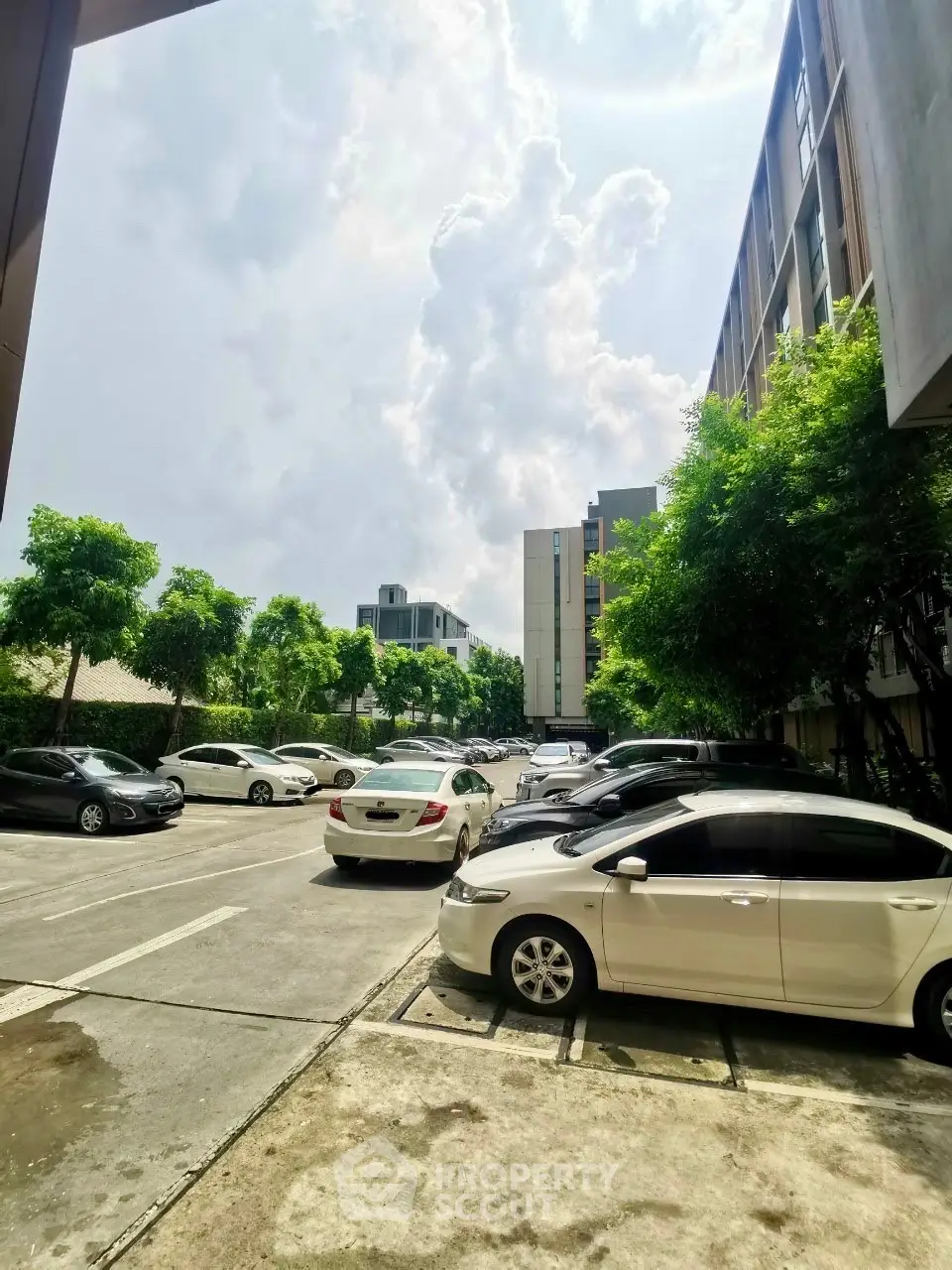 Modern apartment building with spacious parking area and lush greenery under a bright sky.
