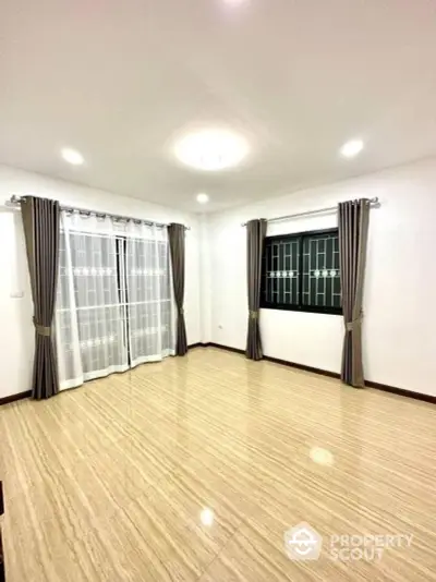 Spacious and well-lit living room with elegant striped curtains and polished wooden flooring, perfect for family gatherings and entertainment.