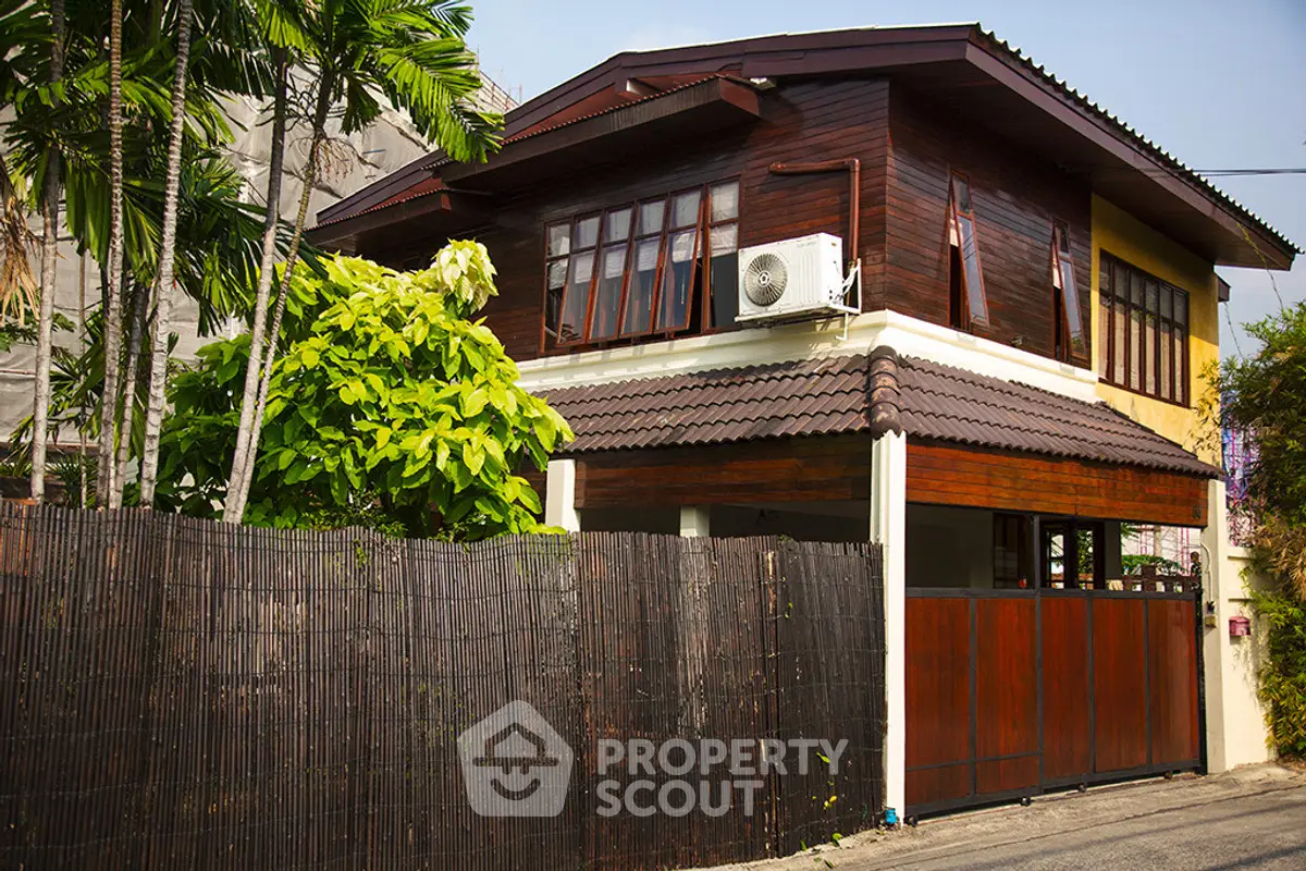 Charming two-story wooden house with lush greenery and a secure fence, perfect for serene living.