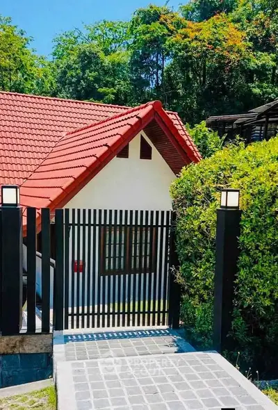 Charming red-roofed house with lush greenery and modern gate, perfect for serene living.