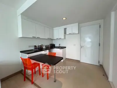 Modern kitchen with sleek cabinets and vibrant orange chairs in a compact layout.