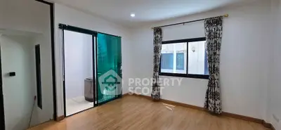 Spacious room with wooden flooring and large window, featuring elegant curtains and glass door leading to balcony.