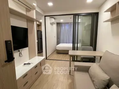 Modern studio apartment with open layout, featuring a cozy living area and bedroom separated by glass doors.