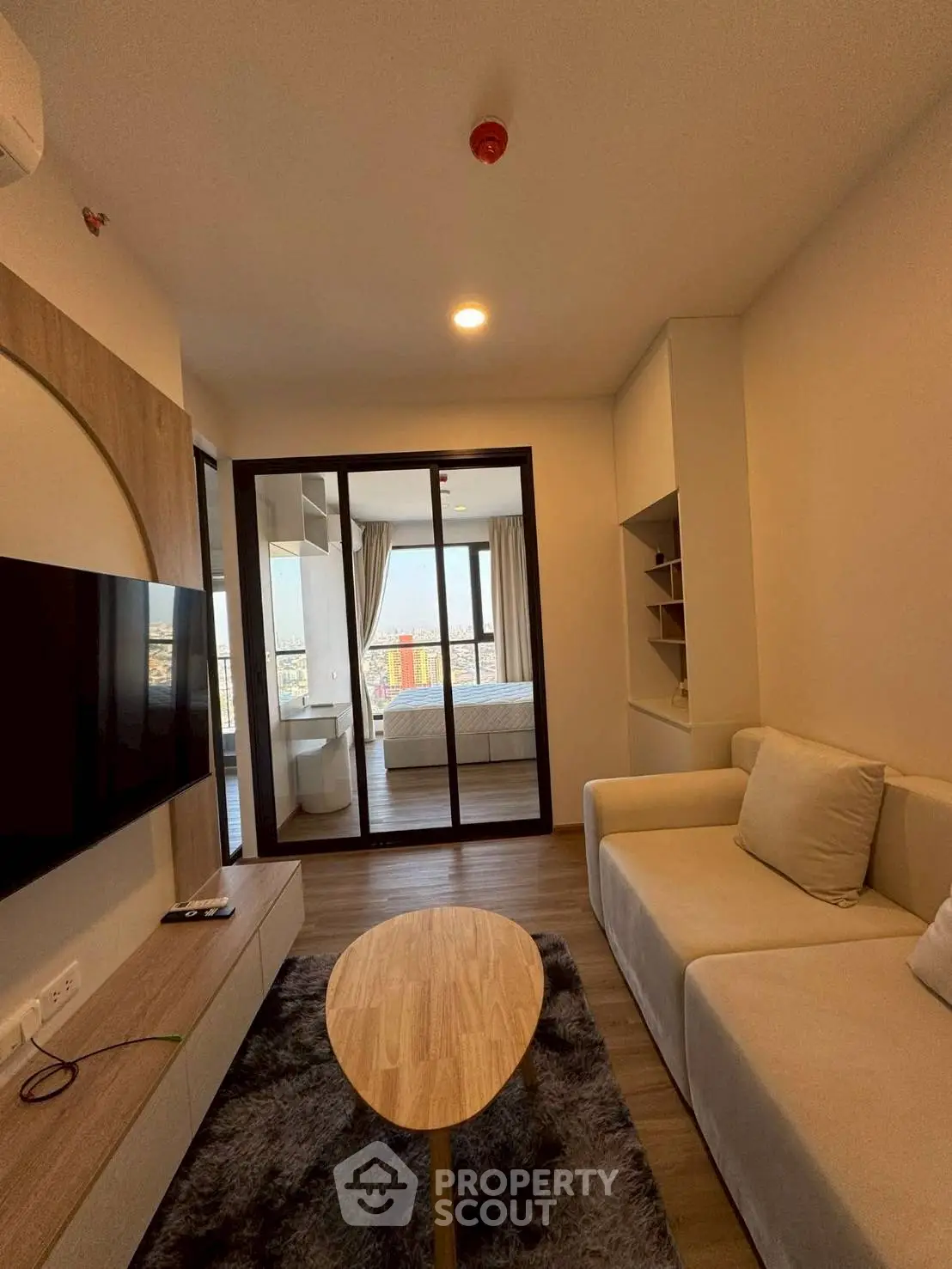 Modern living room with cozy sofa and TV, featuring a view into a stylish bedroom with cityscape.