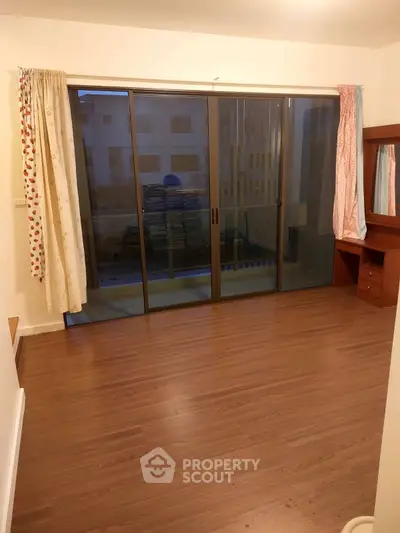 Spacious room with wooden flooring and large sliding glass doors leading to a balcony.