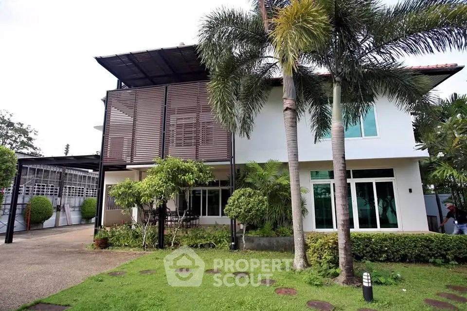 Stunning modern house with lush garden and palm trees, featuring large windows and a spacious patio area.
