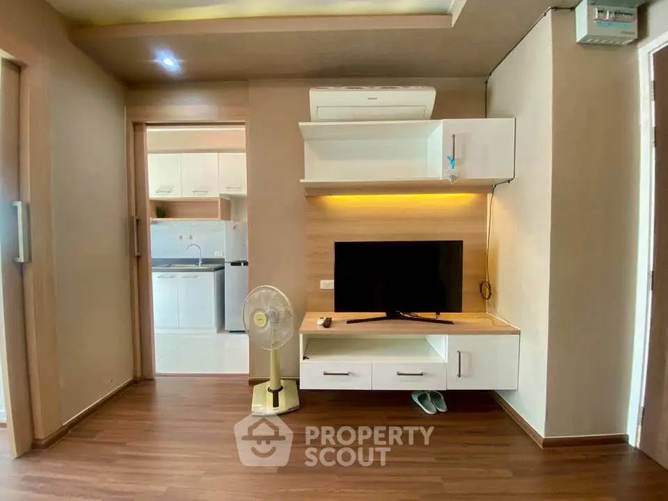 Modern living room with sleek TV unit and wooden flooring, adjacent to a bright kitchen area.