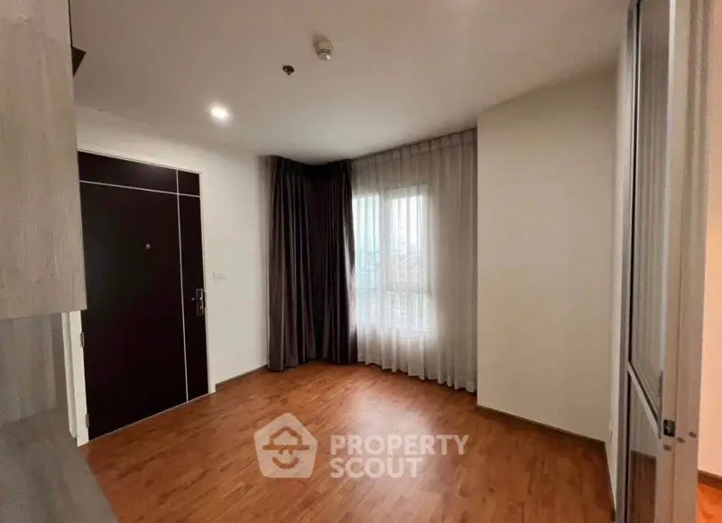 Spacious empty room with wooden flooring and large window, ideal for customization.