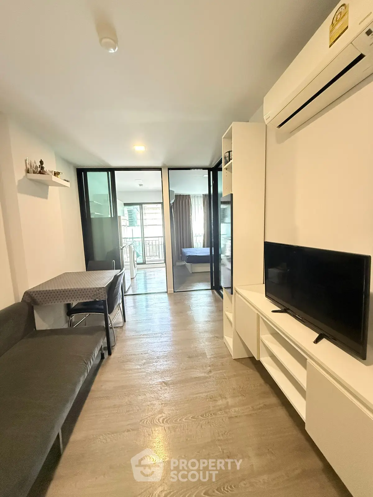Modern living room with sleek design, featuring a TV, air conditioning, and a view into a cozy bedroom.