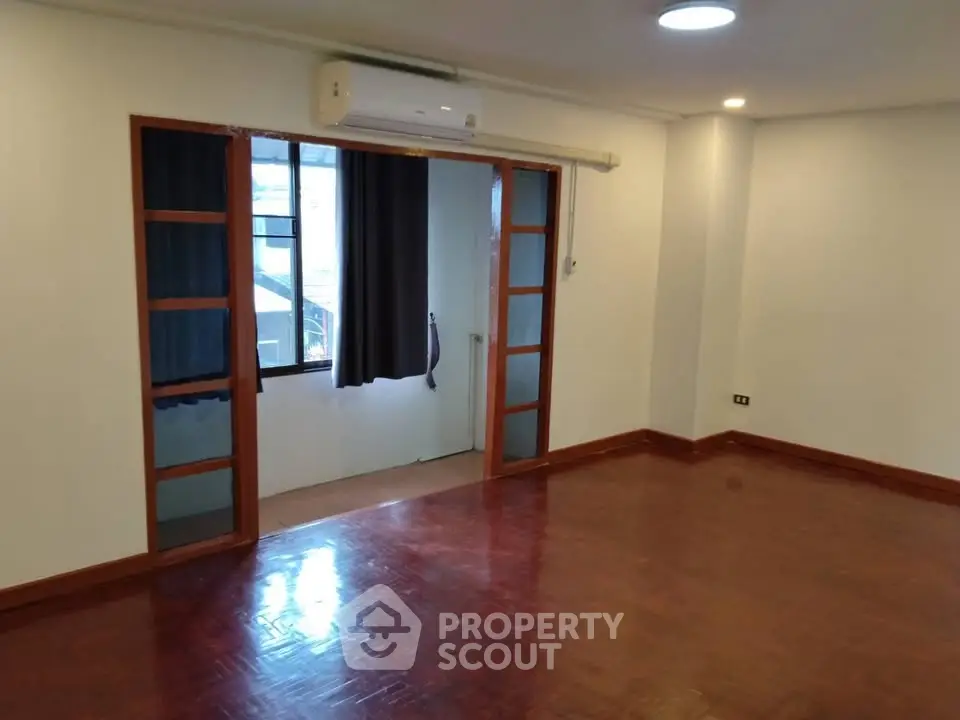 Spacious empty room with wooden flooring and air conditioning, ideal for customization.