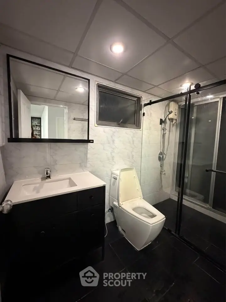 Modern bathroom with sleek black and white design, featuring a glass shower and contemporary fixtures.