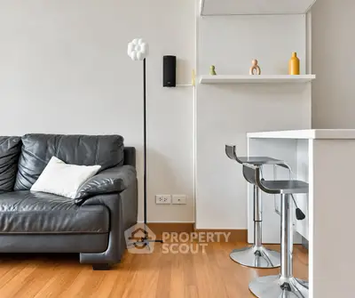 Modern living room with sleek black leather sofa and stylish bar stools in open layout.
