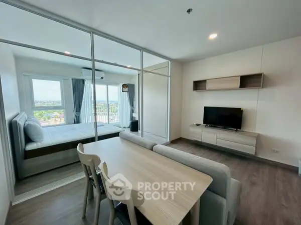 Modern open-plan living room with dining area and bedroom view, featuring sleek furniture and large windows.