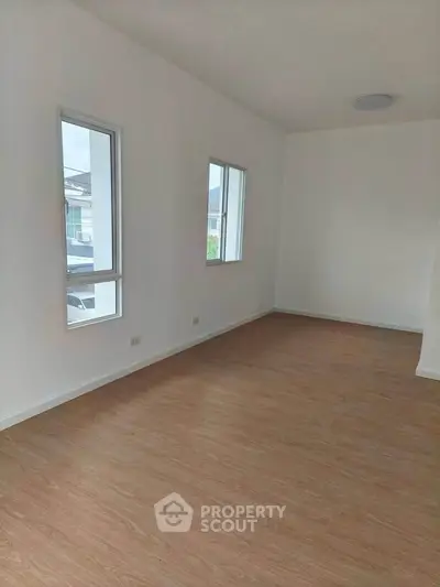 Spacious empty room with wooden flooring and large windows in modern home.