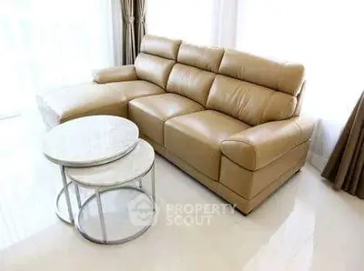 Luxurious beige leather sofa with marble nesting tables in a bright living room.