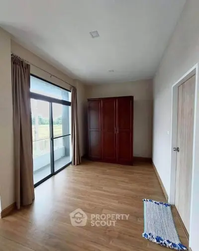 Spacious bedroom with wooden flooring and large window overlooking greenery.