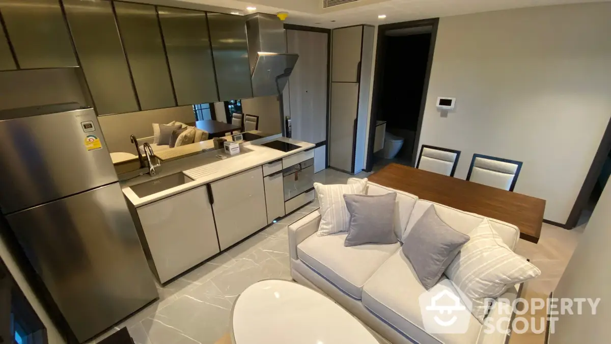 Modern open-plan kitchen with stainless steel appliances seamlessly integrated into sleek cabinetry, adjacent to a cozy living area with plush seating.