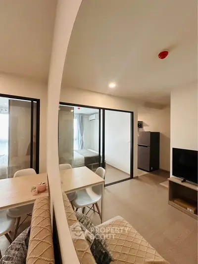 Modern living room with dining area and bedroom view, featuring sleek furniture and contemporary design.