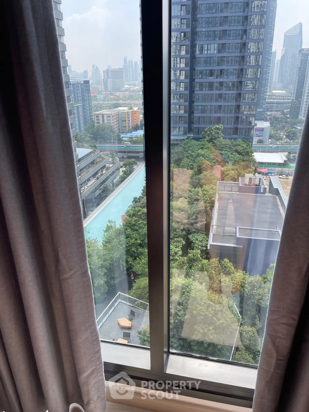 Stunning cityscape view from high-rise apartment window overlooking pool and greenery.