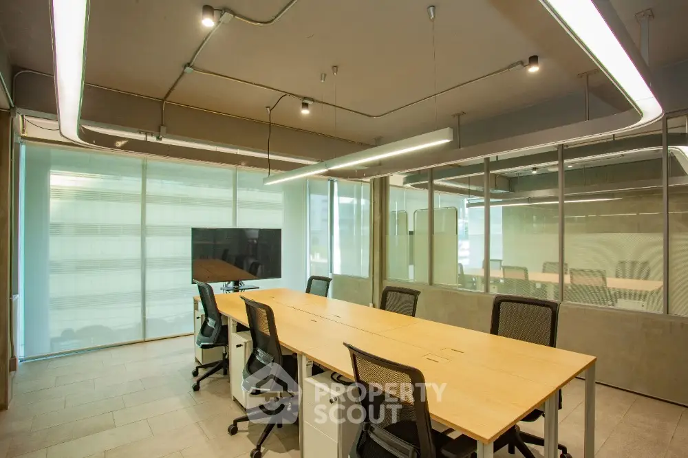 Modern office space with sleek design and ample natural light, featuring a long conference table and ergonomic chairs.