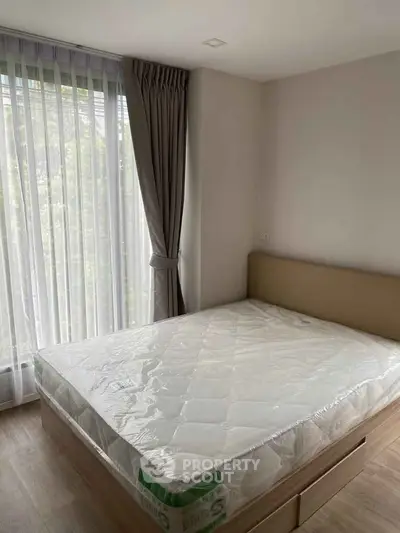 Modern bedroom with large window and natural light, featuring a new mattress and elegant curtains.