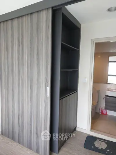 Modern interior with sliding wooden door and built-in shelving, leading to a bathroom with natural light.