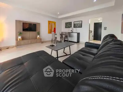 Spacious modern living room with stylish black leather sofa and wall-mounted TV