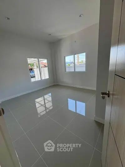 Spacious empty room with glossy tiled floor and large windows offering natural light.