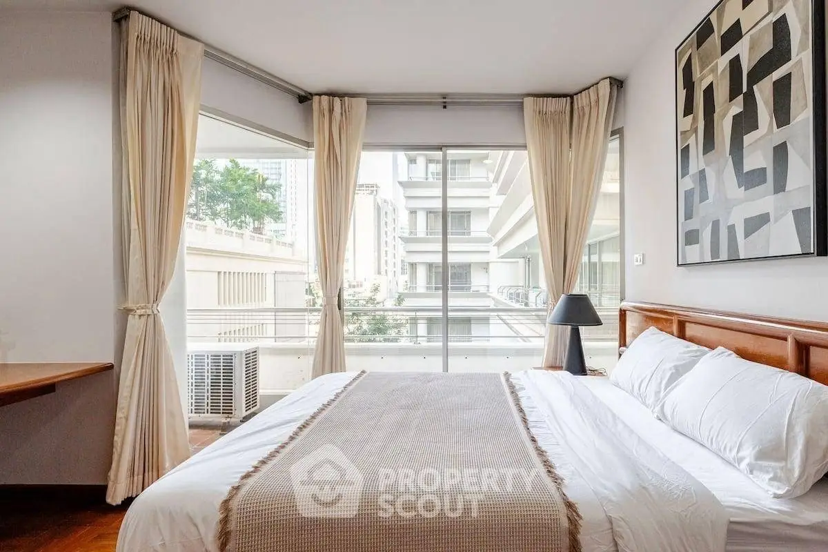 Spacious bedroom with large windows and modern decor in urban apartment.