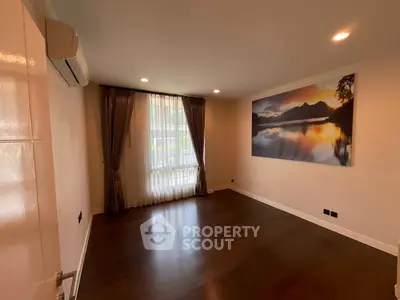 Spacious empty room with wooden flooring and large window, perfect for customization.